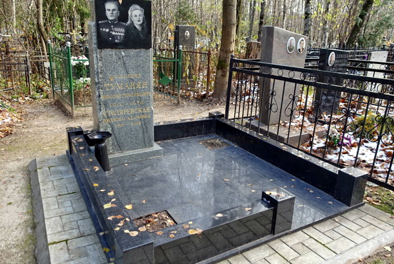 Высокая стела из серого камня и две клумбы без бортов